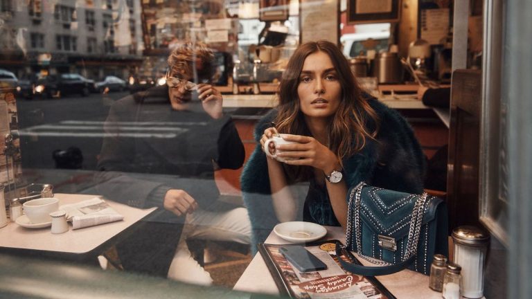 Woman holding a coffee gazes outside the window while sitting inside a cafe