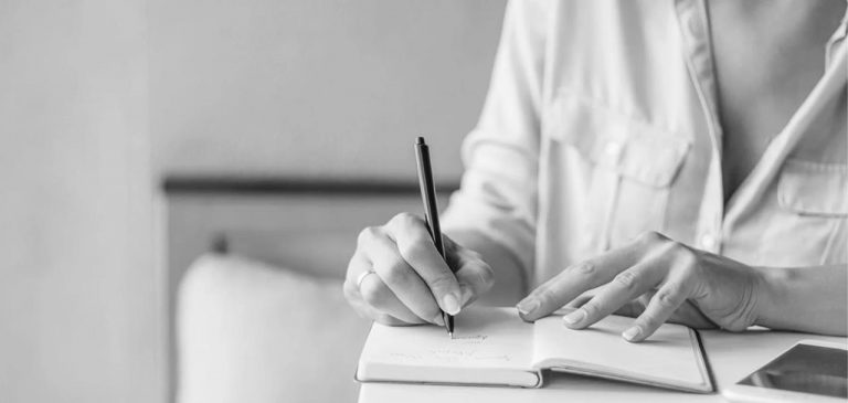 Black and white image of a person writing in a notebook, planning their next career steps