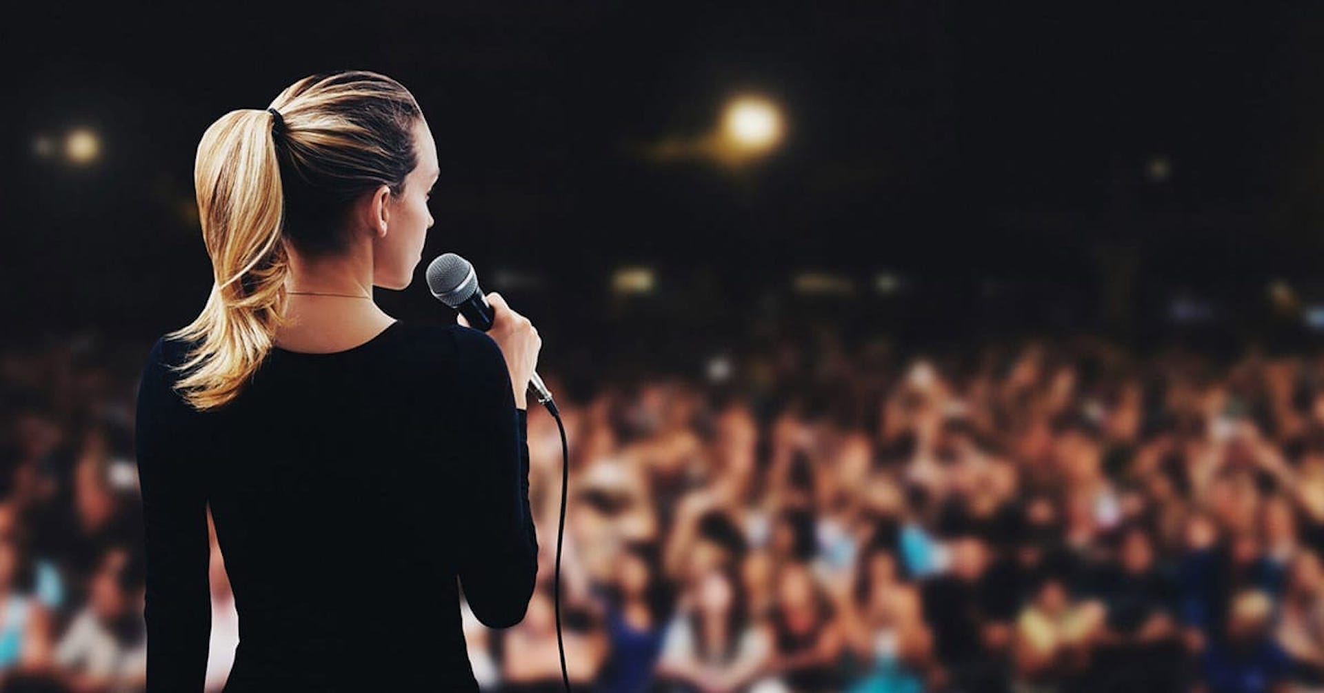Woman with blonde hair doing a presentation to a large audience